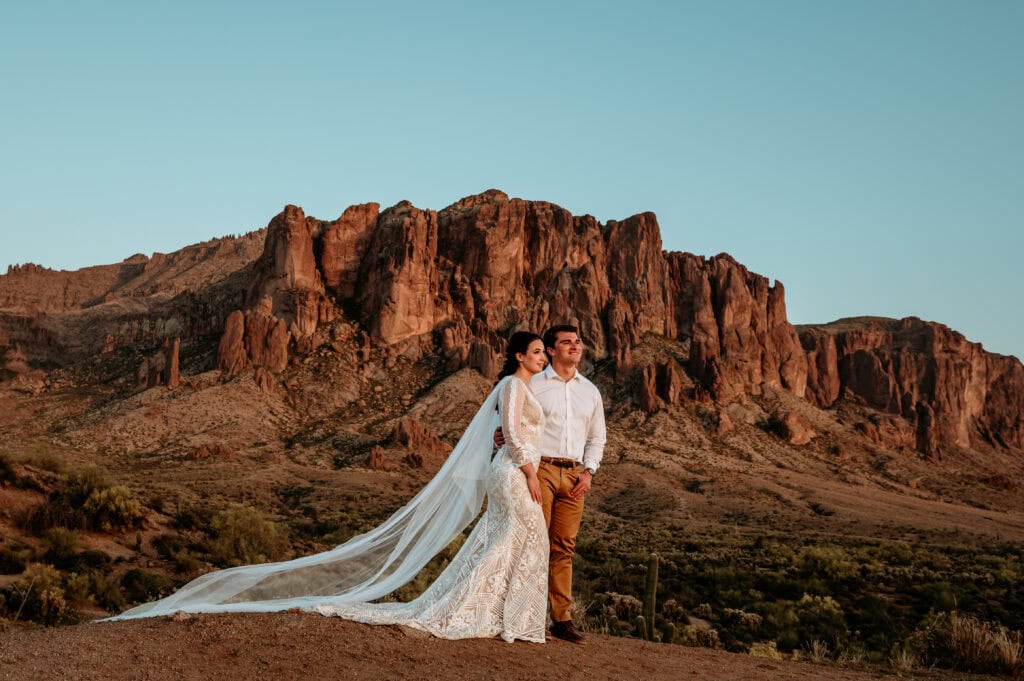 Bride and groom looking towards the sunset with the Superstition Mountains towering behind them during their Phoenix elopement, shot by Stratus Adventure Photography