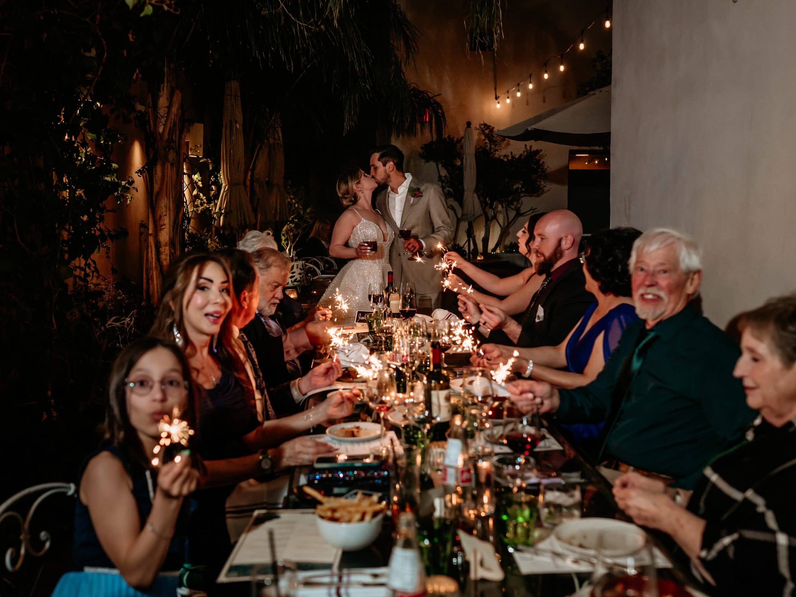 couple kissing at their post elopement dinner with family as family waves sparklers