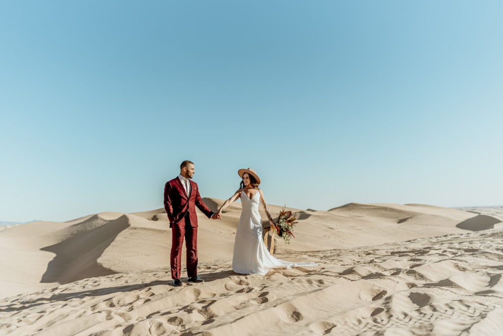 Bride and Groom standing in the desolate desert, surrounded by heaping mounds of golden sand