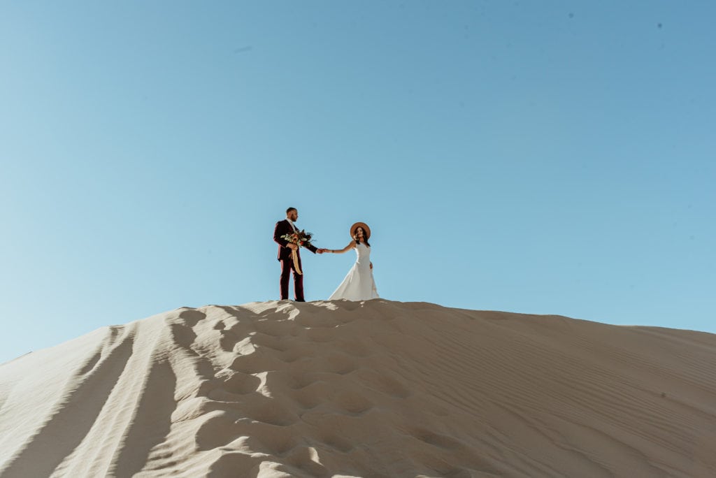 Bride leading groom across a tall sand dune ridge at Glamis Sand Dunes