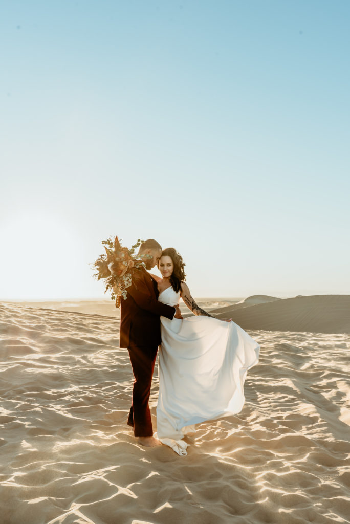 Bride's billowing wedding dress blowing in the desert breeze as her husband holds her at their desert elopement