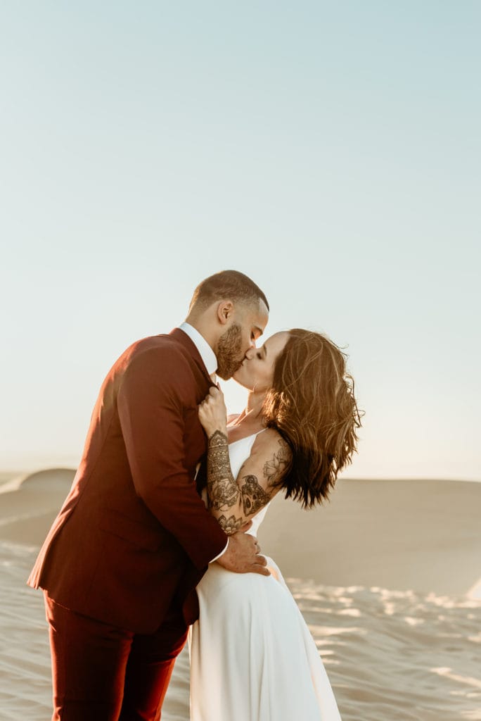 Bride grabbing her husband to her for a passionate kiss by his dark maroon suit