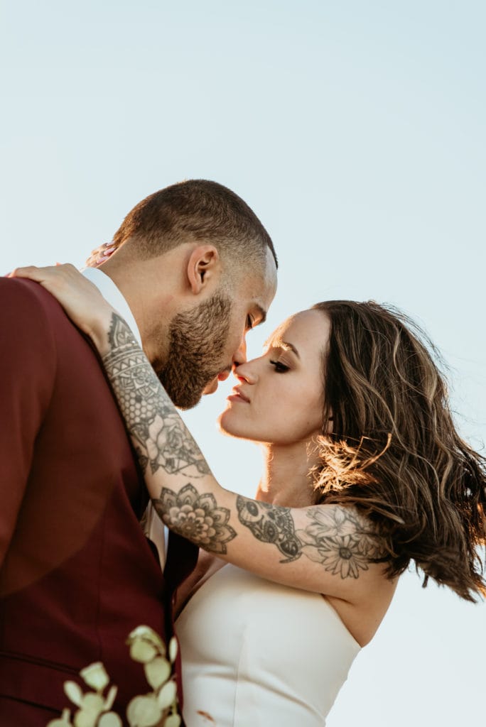 Bride and groom embrace, showing her intricate tattoo sleeve