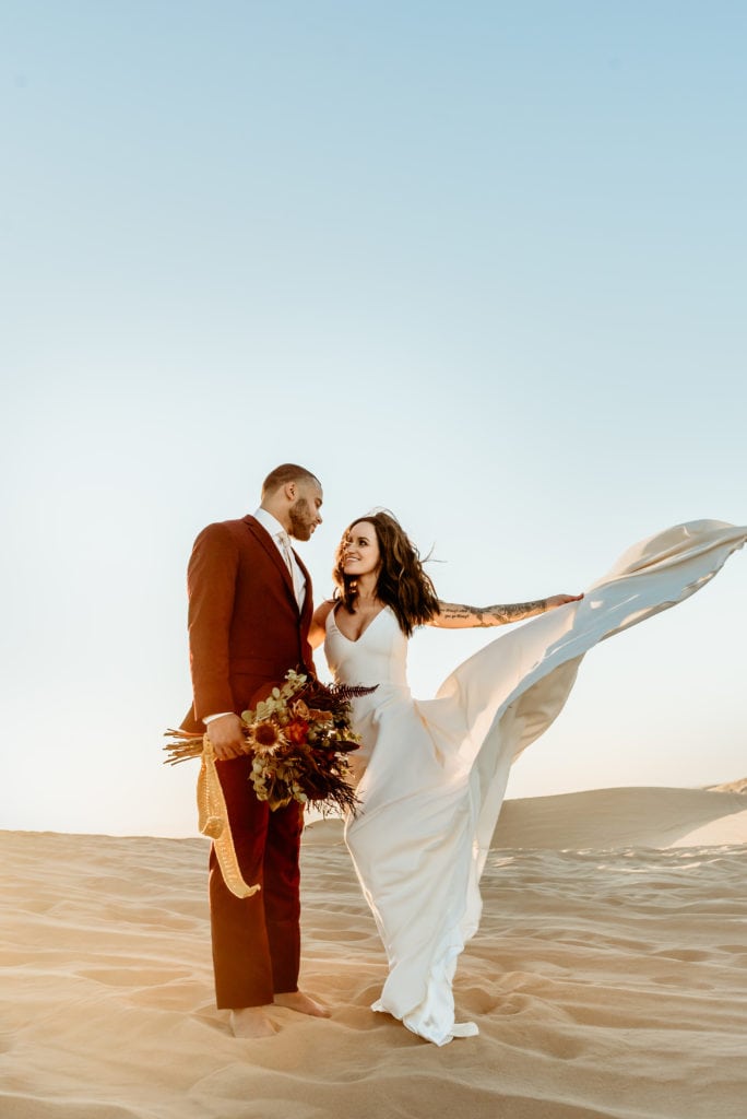 Bride spins her flowing white dress into the sweeping desert wind during their sunset wedding at Glamis Sand Dunes