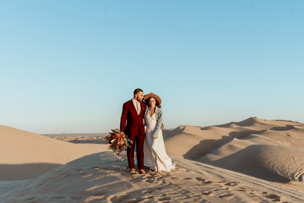 Happy elopement couple standing on a mountain of sand during the sunset