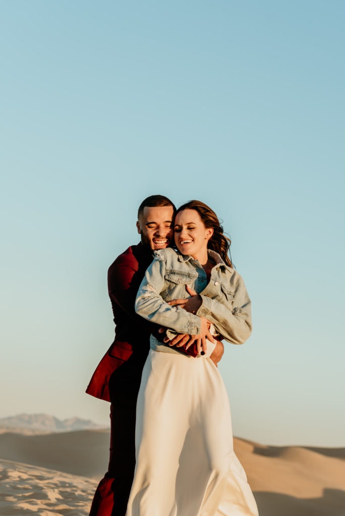 Groom hugs his wife from behind as they laugh playfully