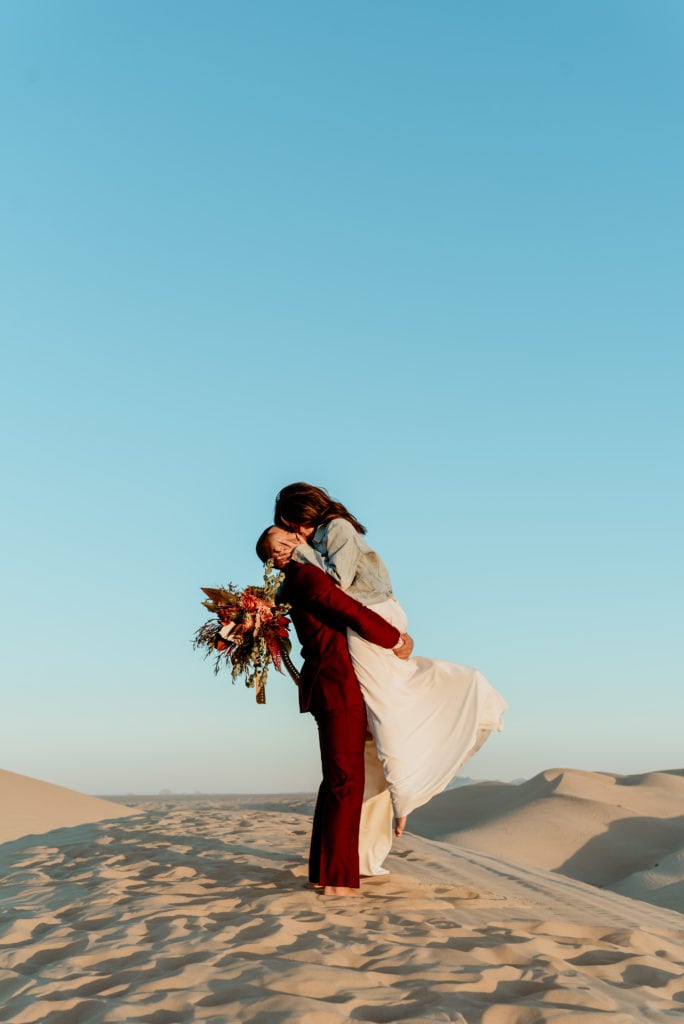 Groom lifting bride in the air during a romantic kiss in the desert