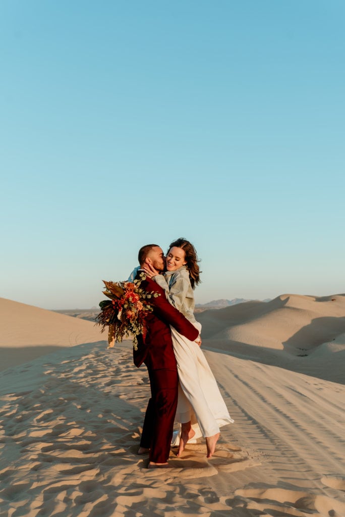 Waves of golden sand as far as the eyes can see behind flirtatious boho wedding couple