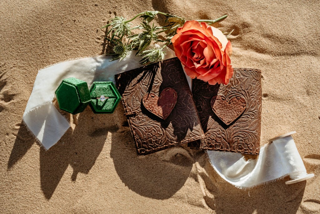 Leather embossed vow books, a deep orange rose, and vibrant ring box show details from this Glamis Elopement