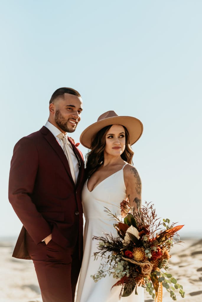 Bride in her boho hat and wildflower bouquet with her husband in a dark red suit at Glamis Sand Dune elopement