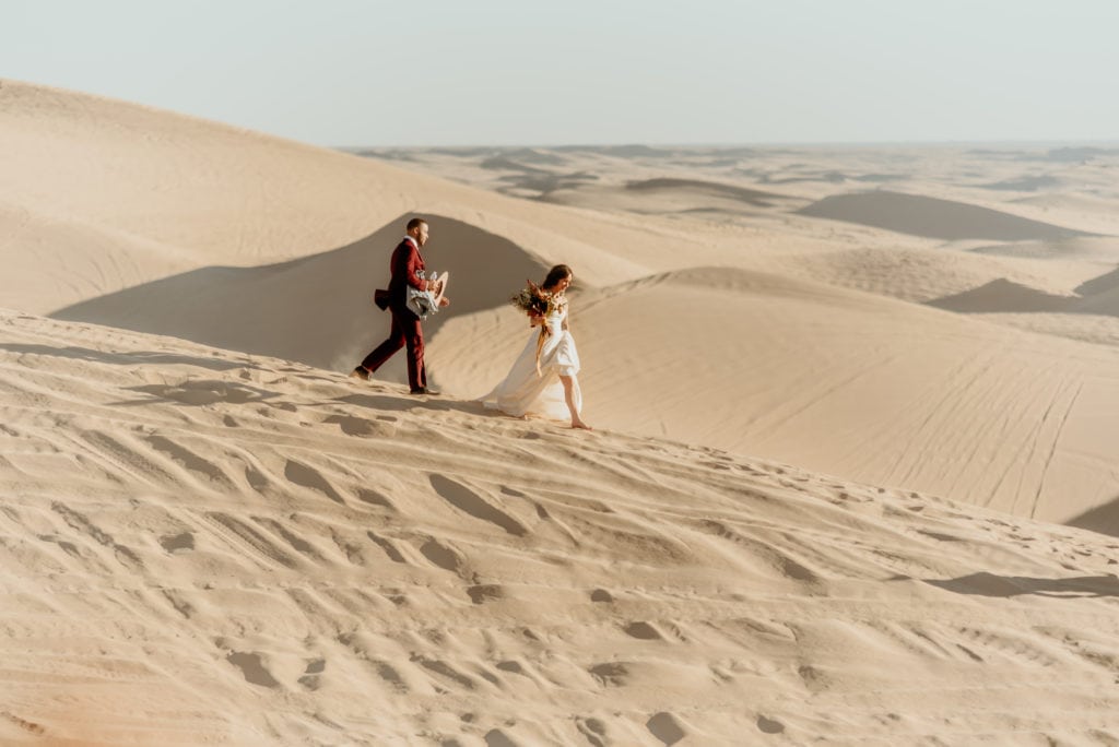 Barefoot couple treks across the barren desert during their Imperial Sand Dune elopmeent