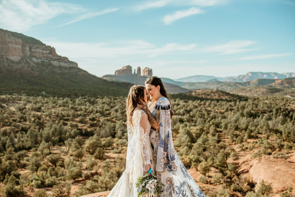 Brides embrace with views of Cathedral Rock in the distance wearing Rue De Seine Dresses