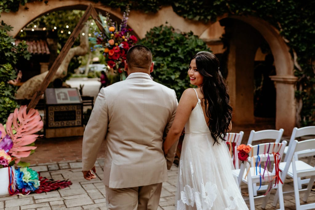 Bride looking over her shoulder as groom leads her down the isle
