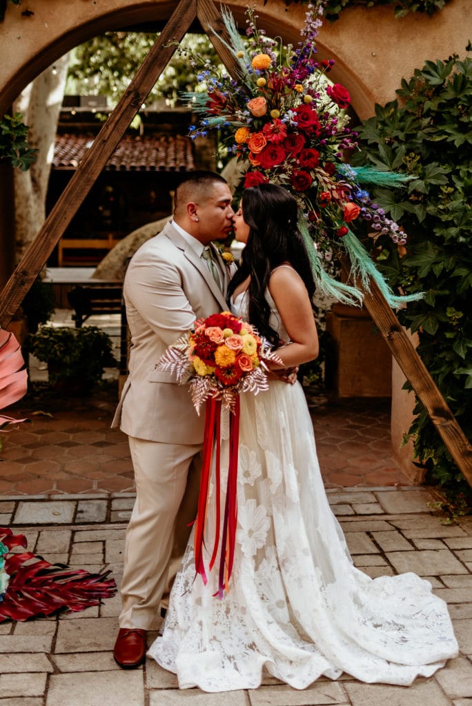 Couple kissing in front of wedding arch at Tlaquepaque