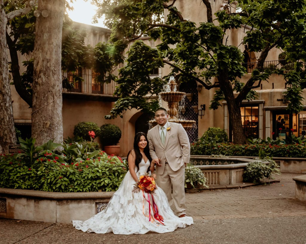 Bride and groom in front of courtyard fountain and trees