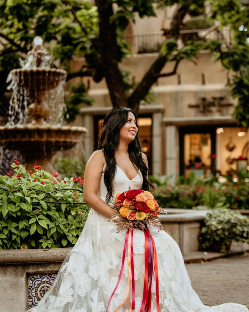 Bride in long flowered lace gown in front of courtyard fountin