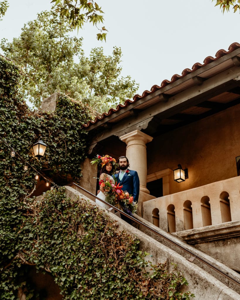 Tropical goddess bride and groom at the top of ivy lined stairs overlooking a stucco courtyard