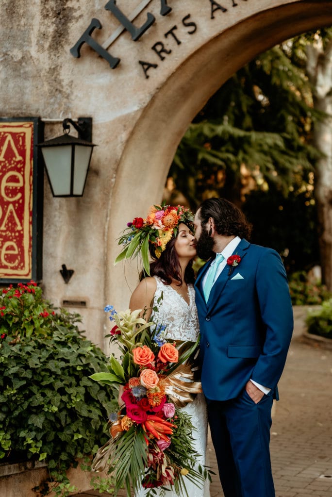 Groom kissing bride holding massive tropical bouquet and headdress