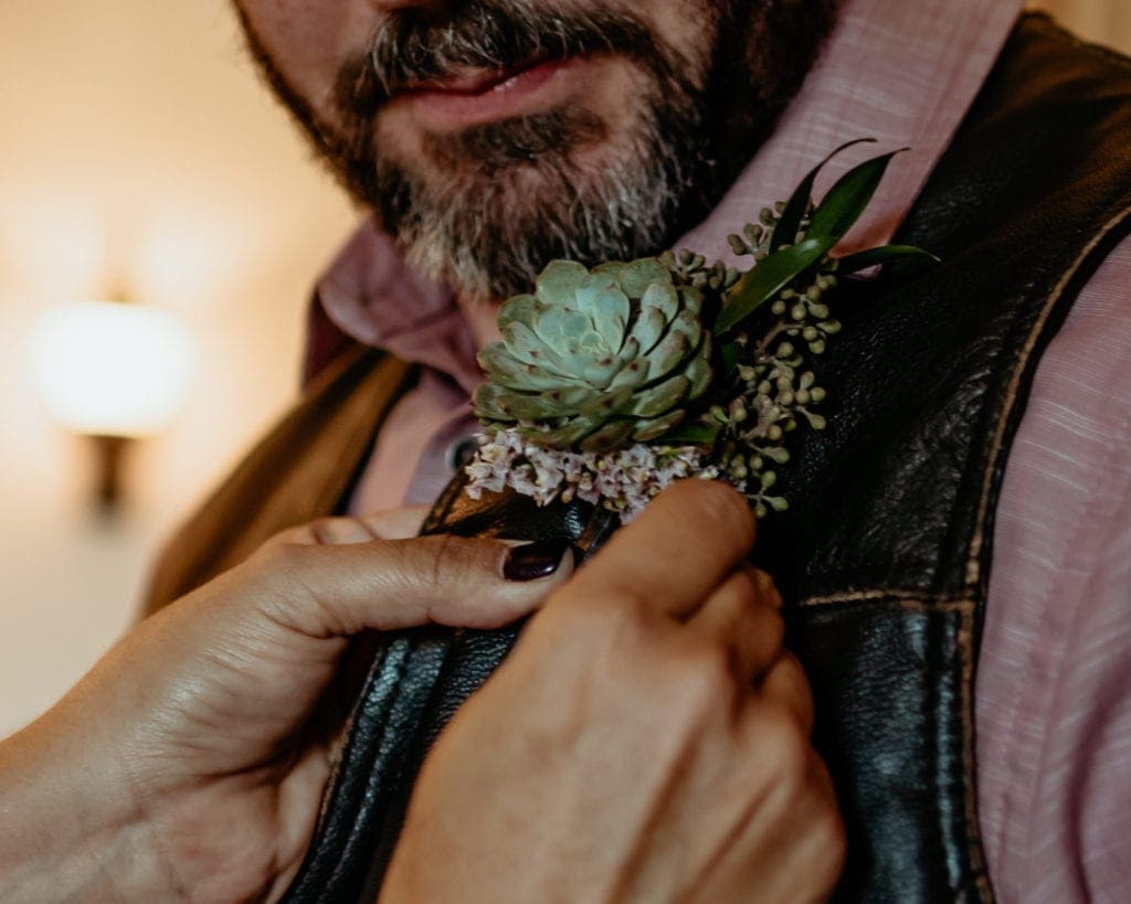 Succulent boutonniere being pinned on grooms leather vest