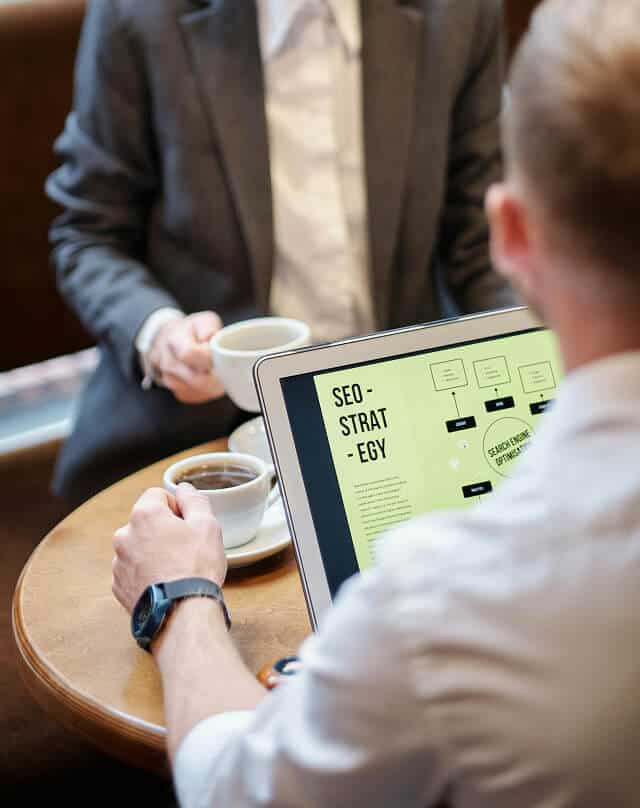 Business professionals discussing SEO strategy and digital optimization on laptop.