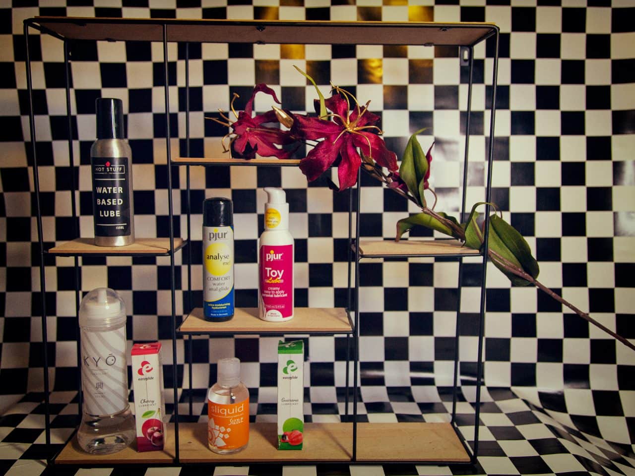 Glijmiddel goed voor een glimlach, een paar planken op een schaakbord achtergrond met op de planken glijmiddel van pjur, sliquid, hot stuff, easyglide en KYO,