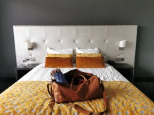 Op een bed in een hotelkamer ligt de bruine leren tas van tom smith. Er steekt zichtbaar wat bondagetouw uit.