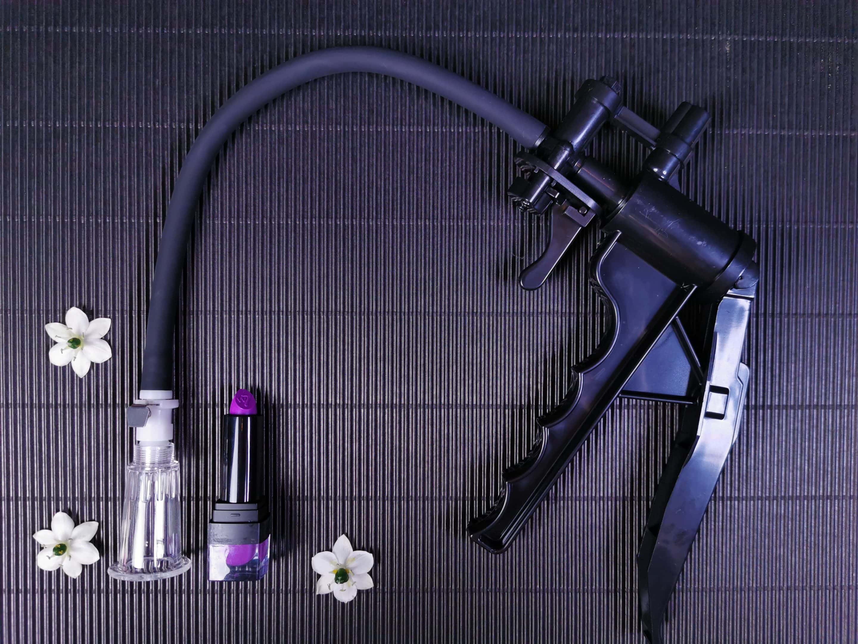 De Saiz Clitoris Pomp Premium ligt op een zwart geribbelde achtergrond, met een lipstick naast het cupje, om het formaat te zien.