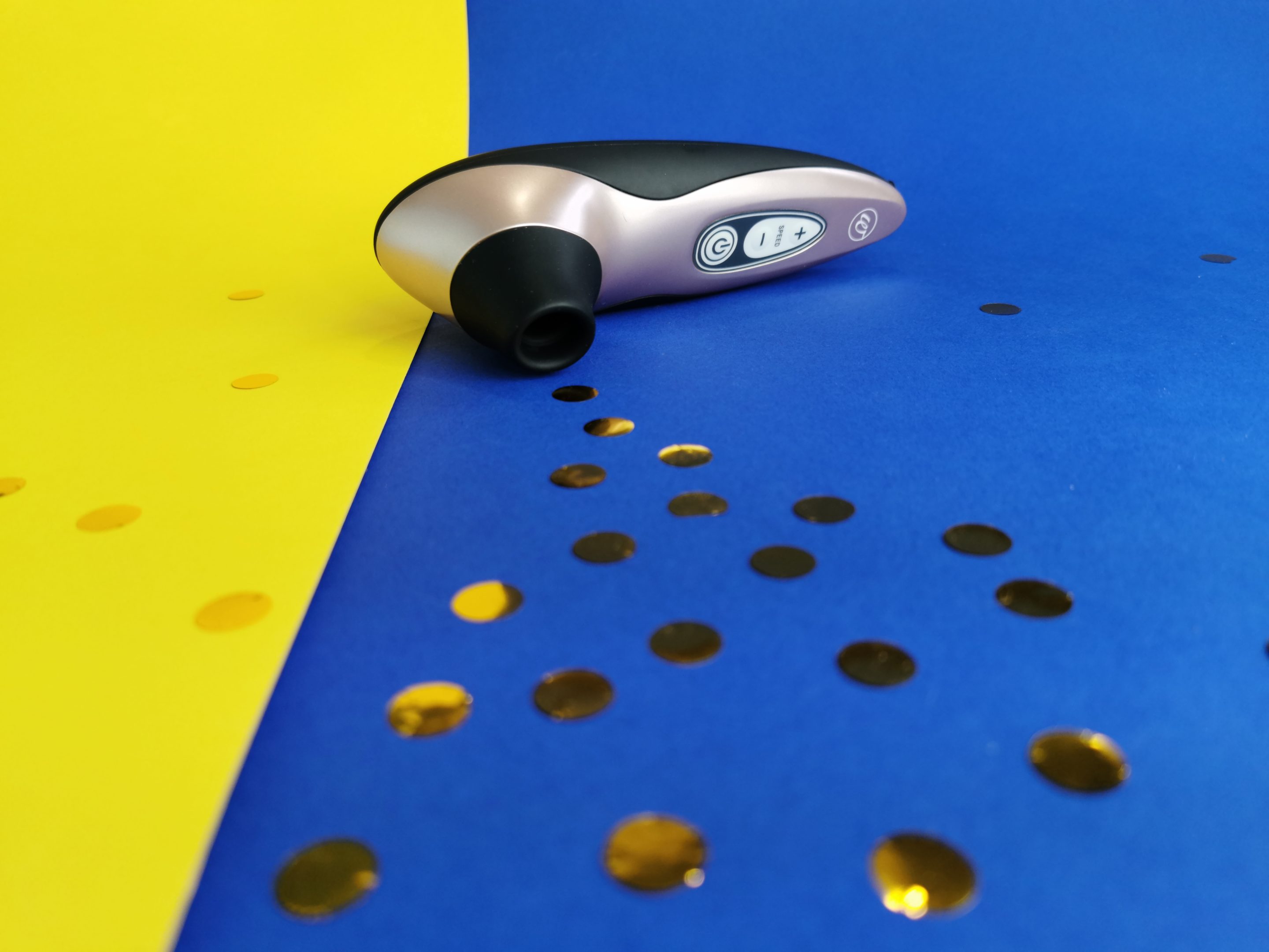 De Womanizer Pro 40 ligt op een geel en blauw achtergrondje. Er licht ook gouden confetti.