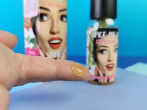 Op de voorgrond mijn vinger met een gele druppel gel, op de achtergrond zie je het flesje happy diva clitorisgel en de verpakking.