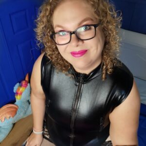 Tess zit op haar knie&euml;n op bed en ze draagt de lovehoney fierce wet look body die je van bovenaf gezien bijna helemaal kan zien. De rits is helemaal dicht en je ziet dat het een beetje trekt aan de bovenkant.