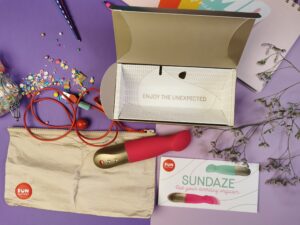 De fun factory sundaze naast de open verpakking. Je ziet ook het beige kleurige bewaar etuitje, het rode oplaadkabeltje en de gebruiksaanwijzing.