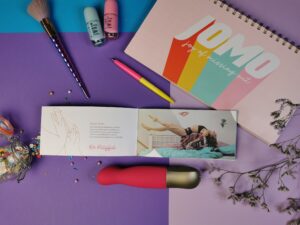 De fun factory sundaze naast de gebruiksaanwijzing die open ligt. Je ziet een foto van een vrouw die boven een bed zweeft, het ziet er heel tof uit.