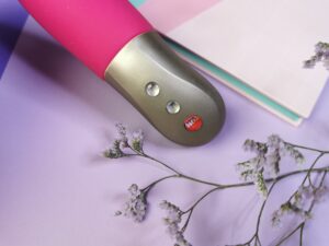 Close-up van de onderkant van de sundaze. Je ziet drie knopjes. Het onderste knopje is rood en er staat fun in. De andere twee knopjes zijn wit en hebben een plus en een min. Het zijn ronde, vrij dikke knopjes.