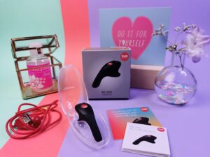 De fun factory be one in de bewaar case, daar achter zie je het doosje met de sleeve er omheen. En je ziet ook de twee boekjes en het rode usb-oplaadkabeltje liggen.