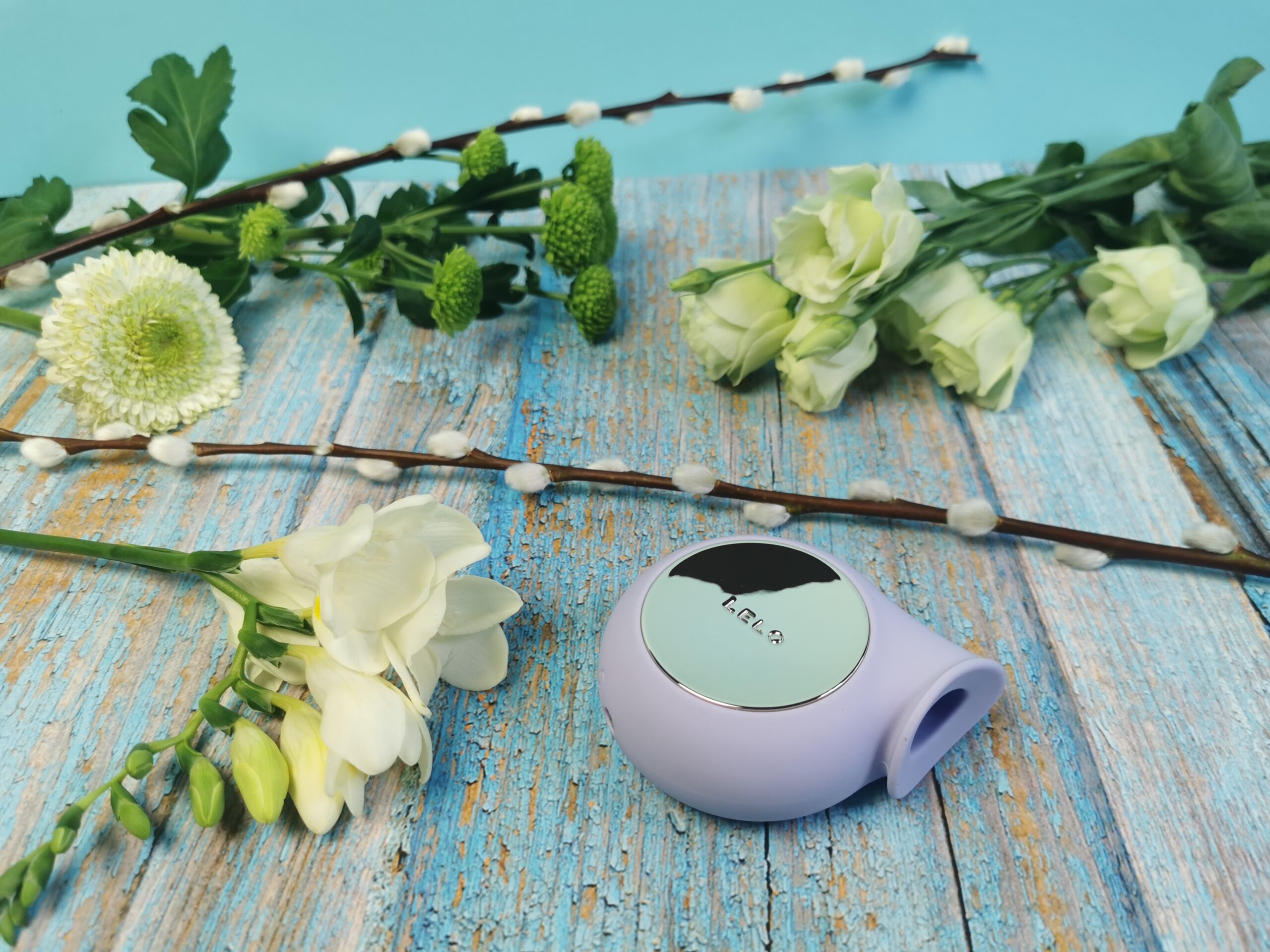 De Lelo Sila ligt op een ondergrondje wat lijkt op lichtblauw geschilderde planken (wat natuurlijk gewoon een kartonnetje is). Er liggen allerlei witte bloemen om de toy heen. De Lelo Sila is een ronde toy met een tuutje, het lijkt een beetje op een slakkenhuis. Het middelste deel van de cirkel is een goudkleurig hard plastic plaatje, met daarin de merknaam Lelo. Het tuutje heeft een aparte opening, die een beetje driehoekig lijkt.