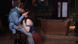 Een still van de film adorn. Parker zit op een kruk en sadie zit op haar knie&euml;n voor hem.