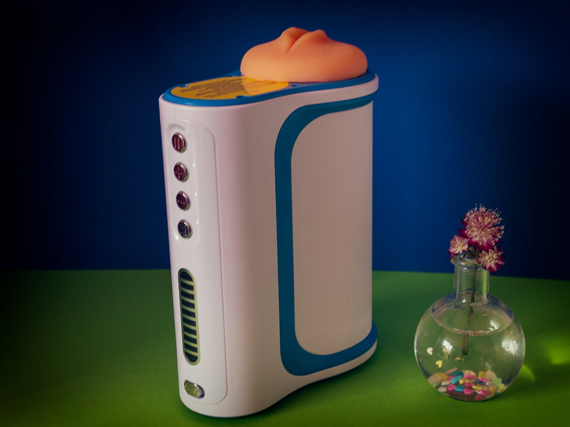 Autblow AI naast een vaasje met een bloem (for scale), de Autoblow is namelijk vrij groot en lomp