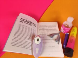 Het boek ligt open, je ziet de tekst: voor je gaat masturberen, nog even dit. Er ligt een womanizer liberty op het boek.