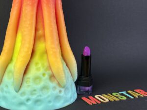 De kiotos monstar dildo beast no. 54 naast een lipstick. Je ziet alleen de onderkant van de dildo omdat 'ie zo enorm is.