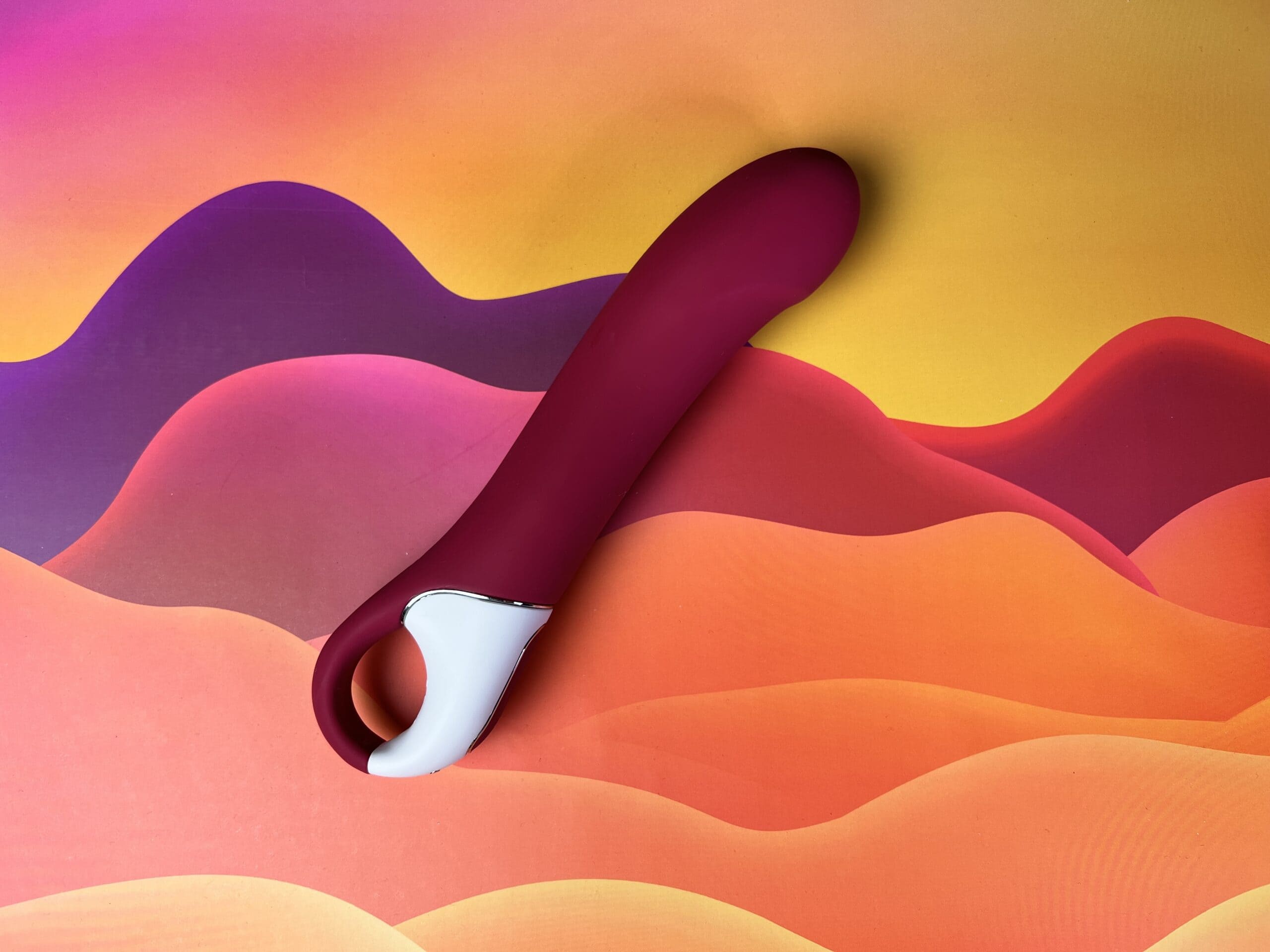 De Satsifyer Big Heat ligt op een gekleurd golvend ondergrondje.