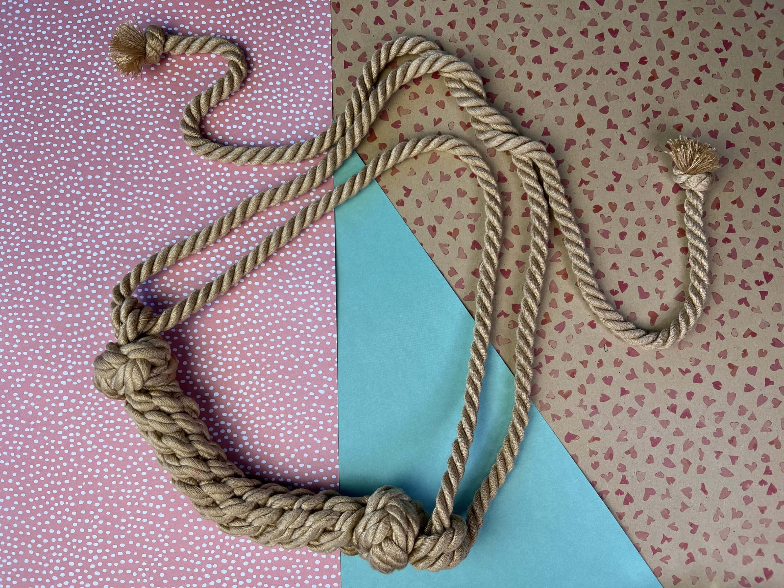 De Shibari Bondage Rope Bite Gag is lichtbruin en soort van gevlochten. Het is een gebogen staafje met daaraan losse touwtjes om 'm vast te knopen.
