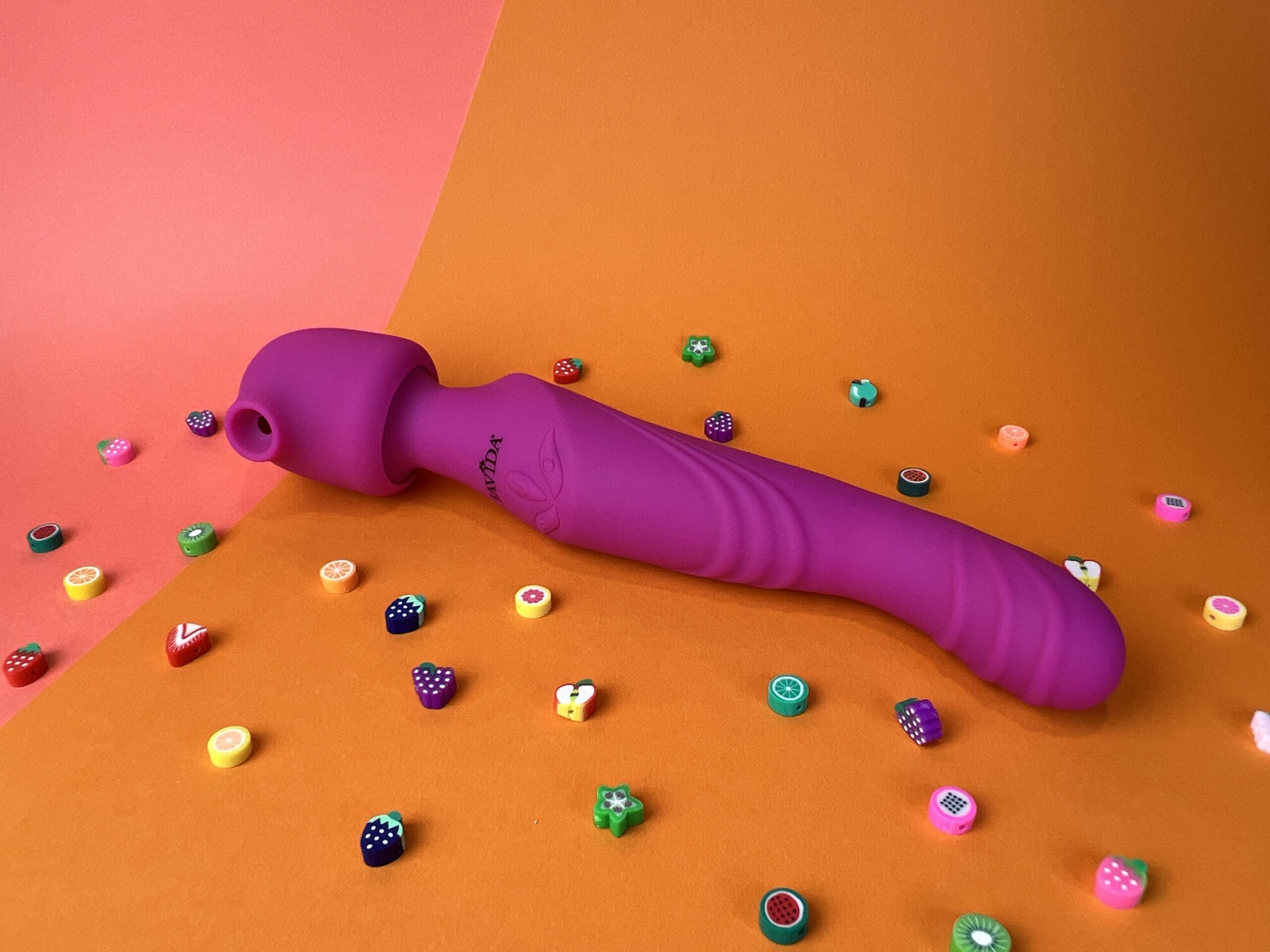 De Javida 3 Function Vibrator op een gekleurd ondergrondje met kraaltjes er omheen. De Javida is roze, lijkt aan één kant op een wandvibrator met tuutje en aan de andere kant is het een G-spot vibrator met wat ribbels.