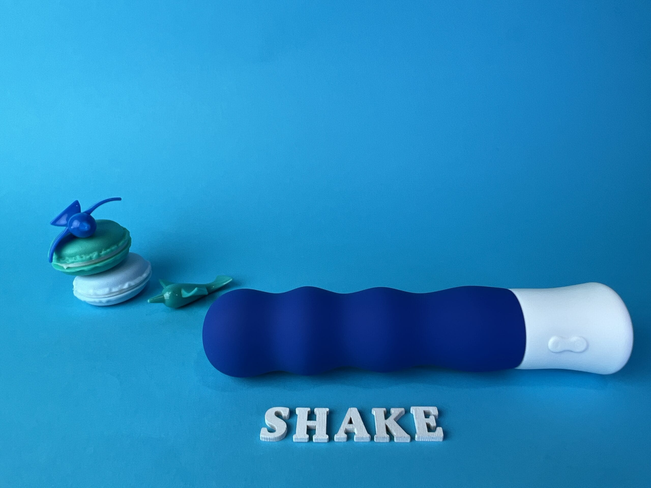 De Inya Shake is een blauwe vibrator met ribbels. Hij heeft een wit handvat. Hij ligt op een blauw ondergrondje.