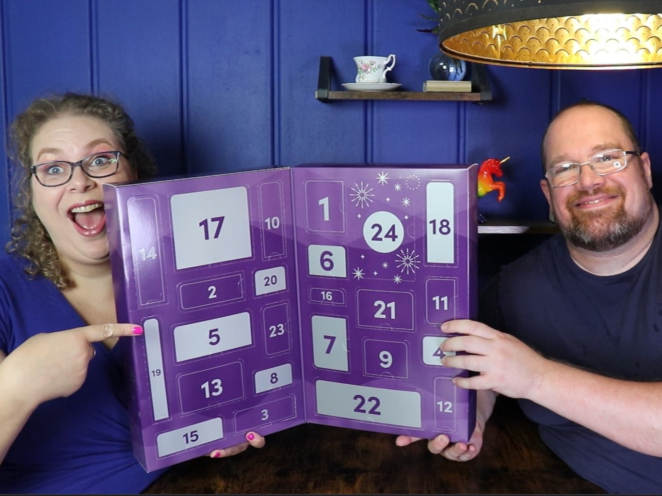 Tess en Jay zitten aan de keukentafel en houden de Lovehoney sextoy adventskalender vast.