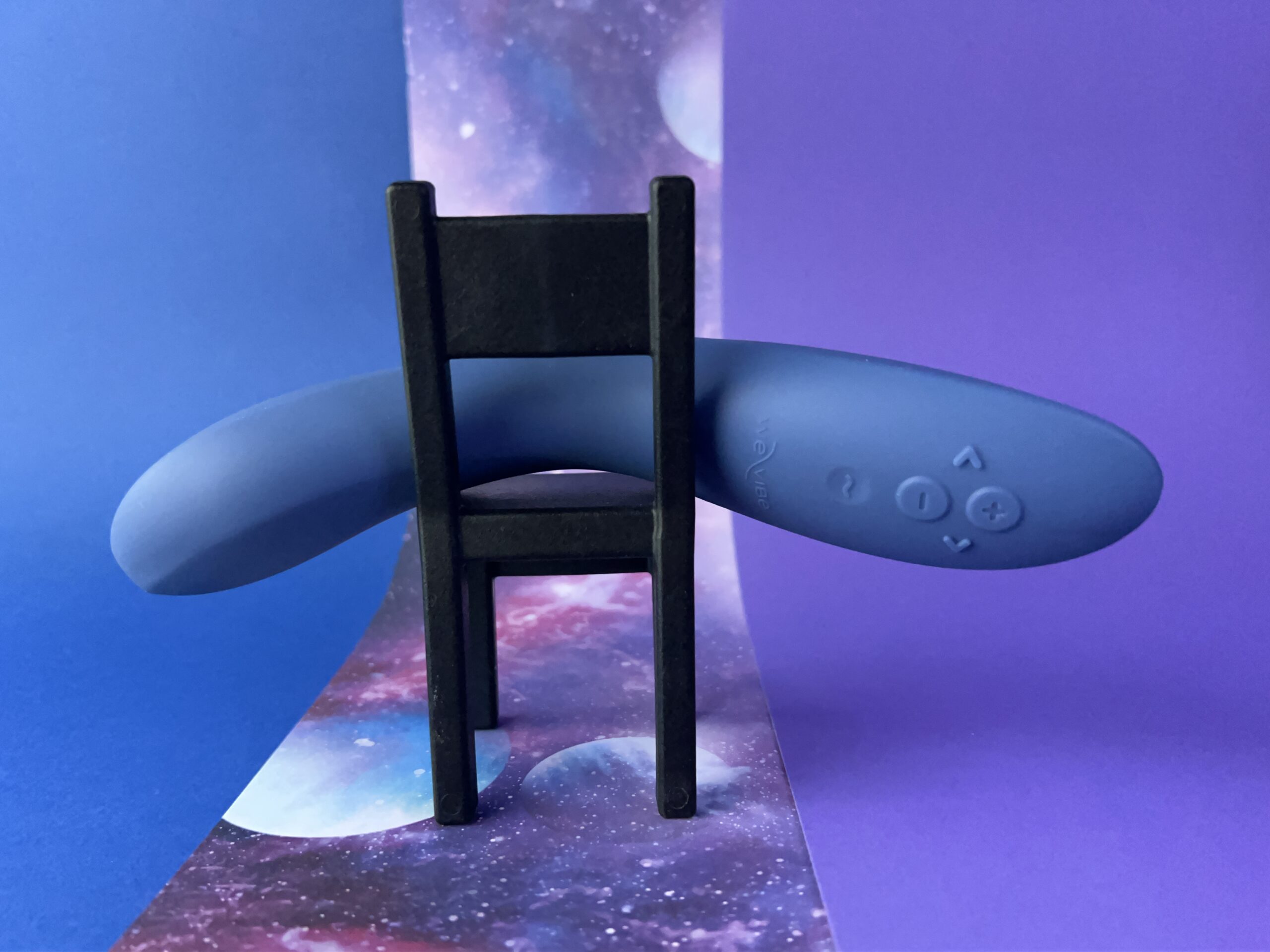 De We-Vibe Rave 2 ligt op een omgekeerd min stoeltje, de achtergrond is blauw, paars en galaxy.
