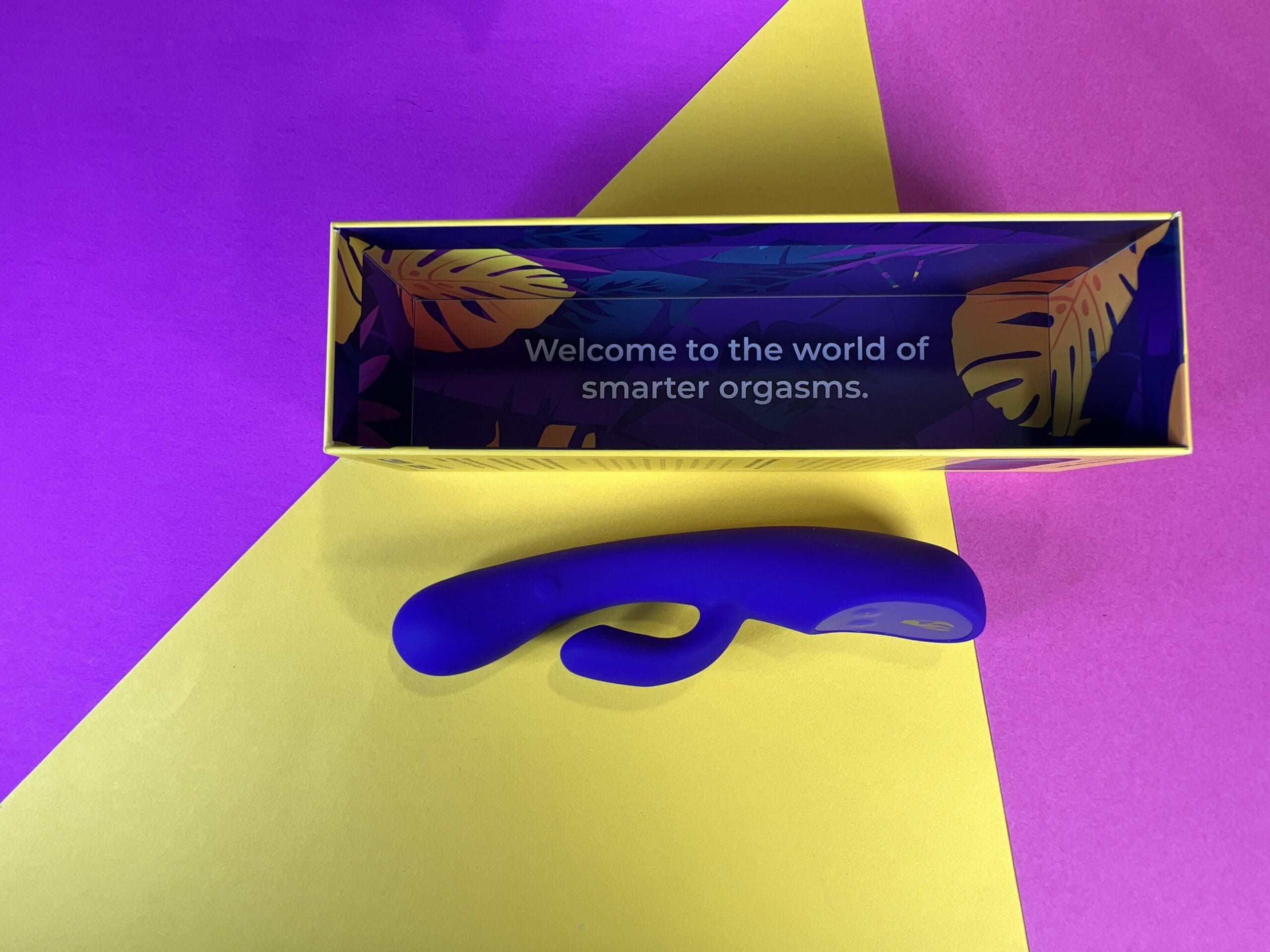 Je ziet de Lioness Smart Vibrator op een paars, geel, roze ondergrondje. Er boven kijk je in de binnenkant van de verpakking. Je ziet daar de tekst 'Welcome to the world of smarter orgasms' in staan.