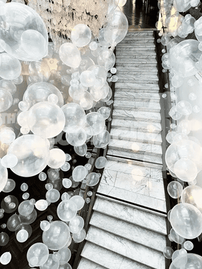 A marble staircase in Los Angeles is adorned with elegant balloon decor—translucent white balloons of various sizes create a stunning, floating effect along the stairs and surrounding area.