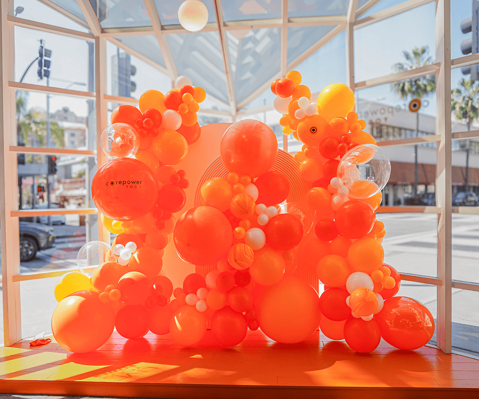 Bright orange and white balloon decor displayed indoors by large windows, with Los Angeles streets and palm trees visible outside.