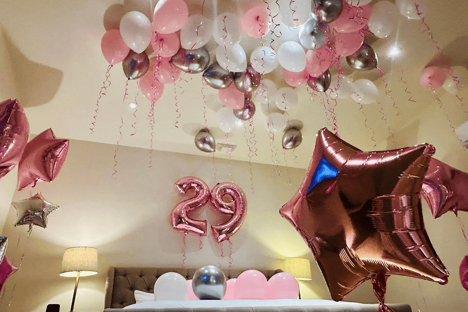 A bedroom decorated with pink, silver, and white balloon installations, including a large "29" balloon above the bed, marking a 29th birthday celebration.