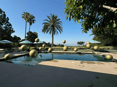 Outdoor pool in Los Angeles surrounded by palm trees and lounge chairs, with several large gold balloon installations floating above and around the water.